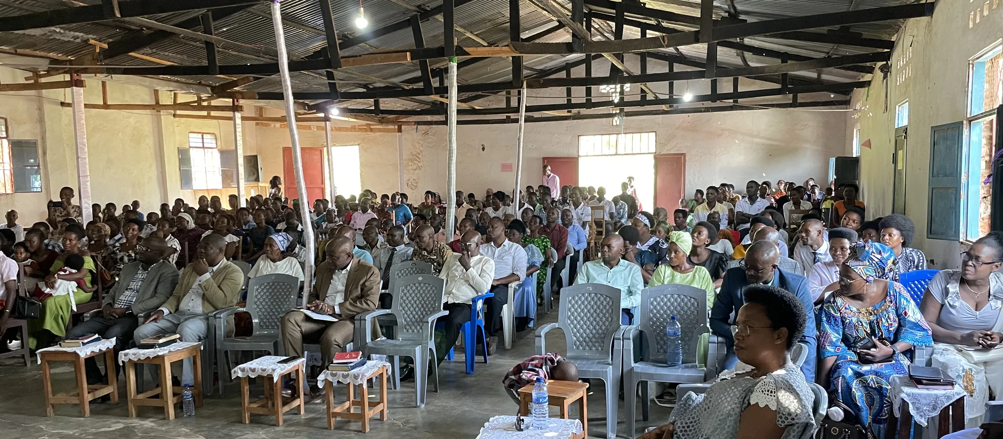 The congregation at Gasenyi filling a tin-roofed church, seated on plastic chairs and wooden benches