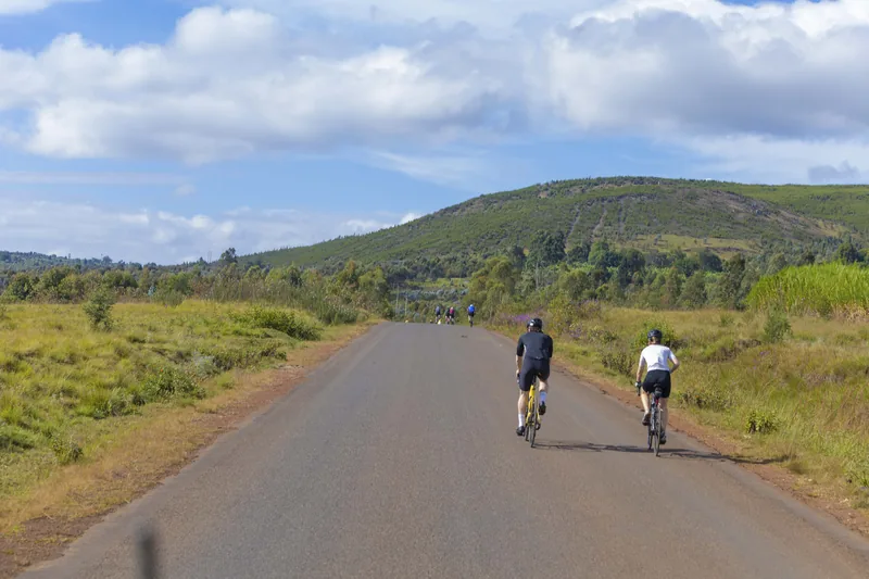 An empty road running out towards green hills, two riders small against it